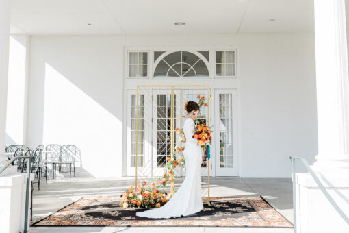 Bride standing on a large ornate rug with a gold backdrop posing for wedding photos