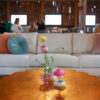 Gold metal coffee table with scallop edges in the foreground and a white soft in the background against a wooden barn wall.