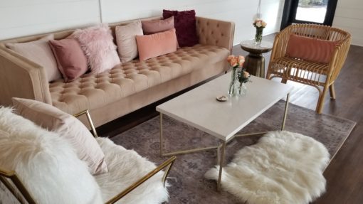 Lounge seating rentals featuring a pink sofa with pillows, a white coffee table, a modern rug, rattan chair, and dramatic white chair
