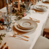 Romantic table setting for wedding reception with gold and white plates, vintage gold flatware, blue goblets and florals