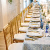 Long table at the head table at wedding with gold chairs, blue table cloth and blue goblets