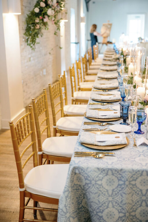 Long table at the head table at wedding with gold chairs, blue table cloth and blue goblets
