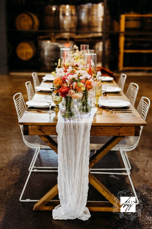 Warm wooden farm table with white wire chairs, orange hues on florals.