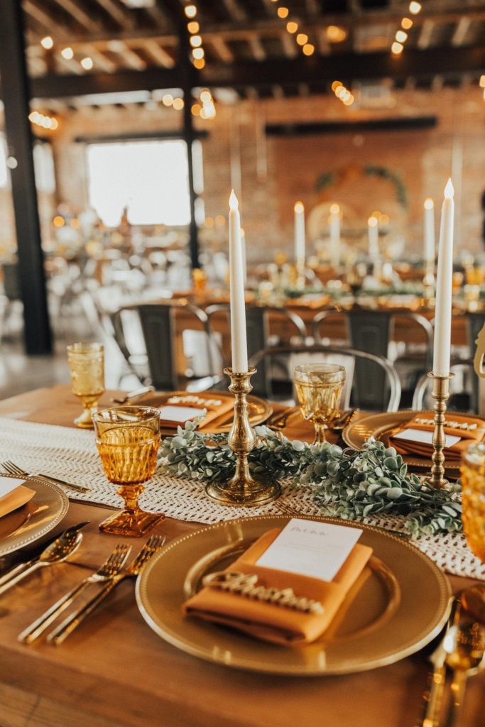 wedding reception table with brass candlesticks, gold chargers, and mismatched amber goblets