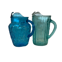 Two vintage pitchers next to each other. One is more rounded and primary blue. The other is skinny and slightly teal.