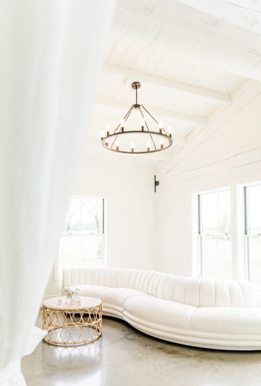 Partial view of white sectional, curved. Natural light coming through windows behind. Hanging circular light.