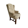 Tan high back wing chair with button tufting and nail head trim on arms. Dark wood legs. Side angle