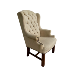 Tan high back wing chair with button tufting and nail head trim on arms. Dark wood legs. Side angle