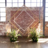 Diamond shape backdrop against exposed brick wall and big industrial windows. Green florals in front with lots of natural light.