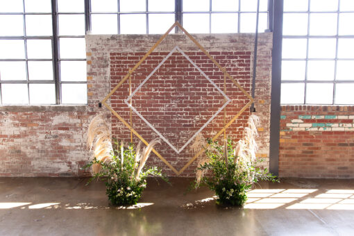 Diamond shape backdrop against exposed brick wall and big industrial windows. Green florals in front with lots of natural light.