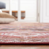 4x6 foot rug with floral patterns around boarder and design in the center. Hues of red with blue, cream and other neutral hues. Flat rug showing low pile.