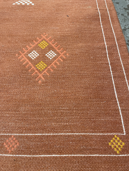 Close up of the white line border on the rug. Orange and yellow diamonds around the edge.