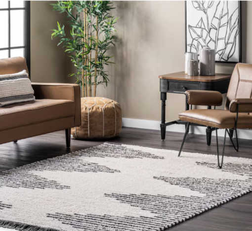Beige and gray geometric rug on the floor with brown leather sofa and arm chair. Leather pouf and tree in the corner.